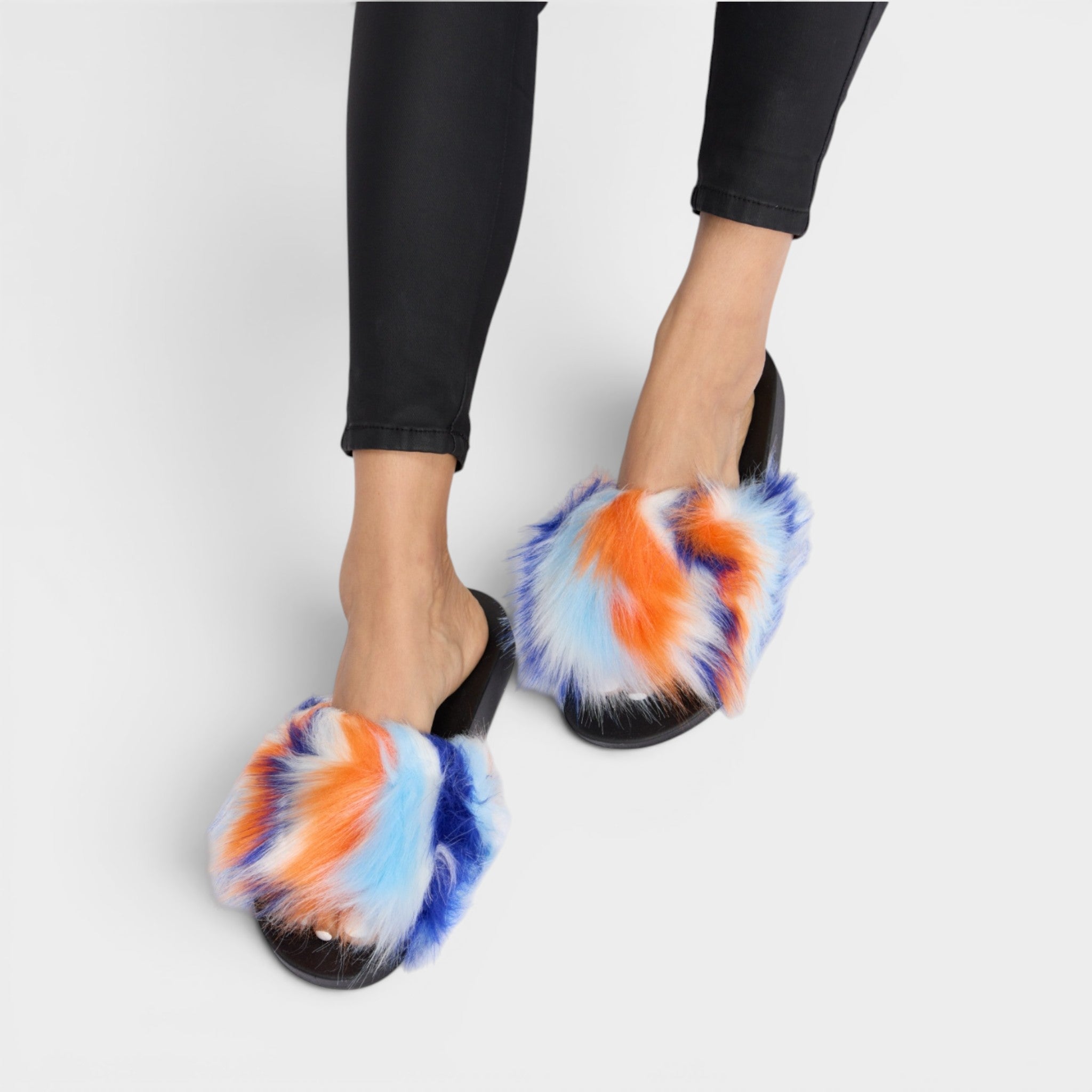 Colorful fluffy slippers worn with black pants on a light gray background