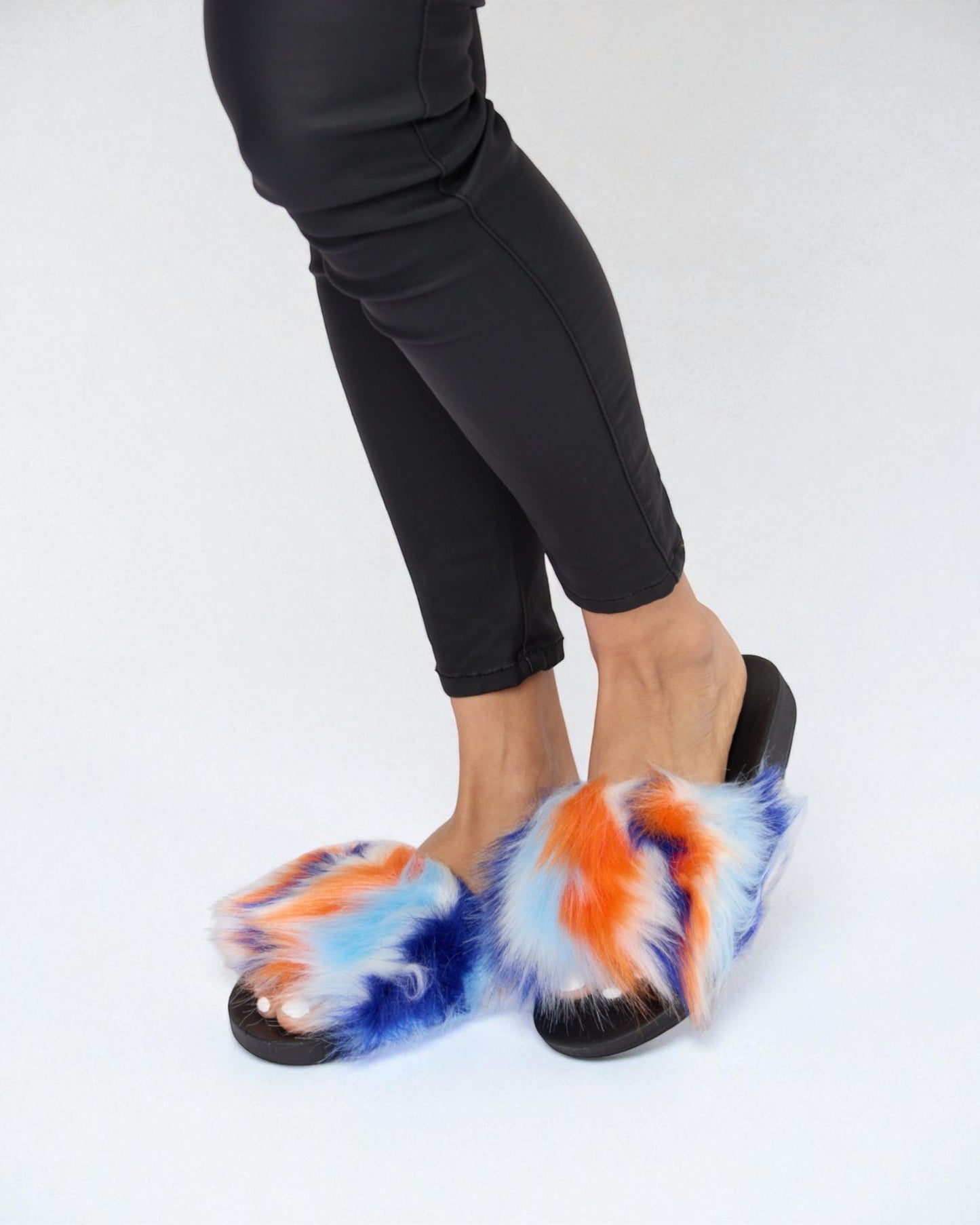 Multicolored fuzzy slippers worn with black pants on a white background