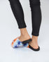 Person wearing tie-dye sandals with black straps on a white background