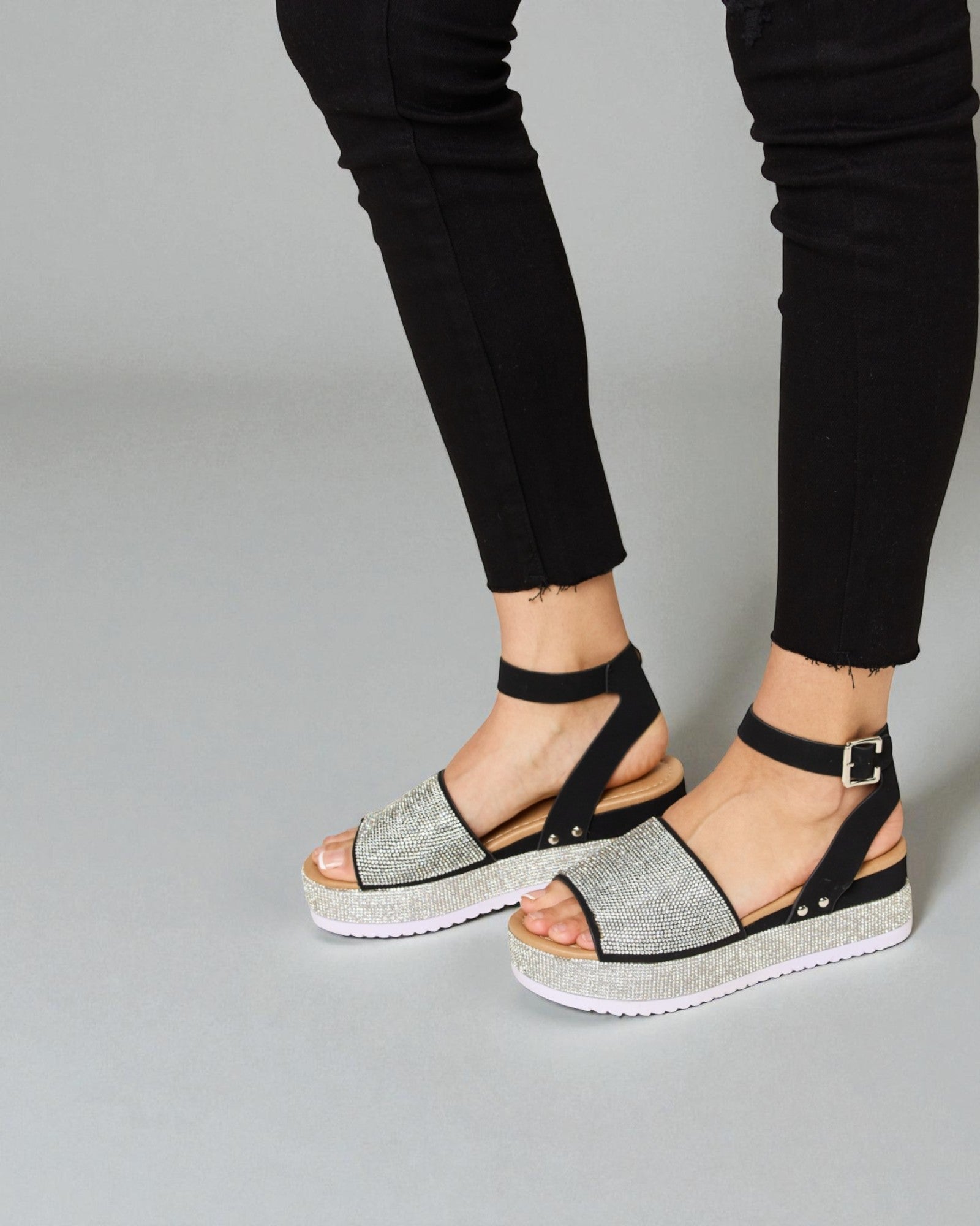 Black sandals with glittery platform sole worn with black pants on a gray background