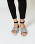 Silver open-toe sandals with black straps worn with black pants on a white background