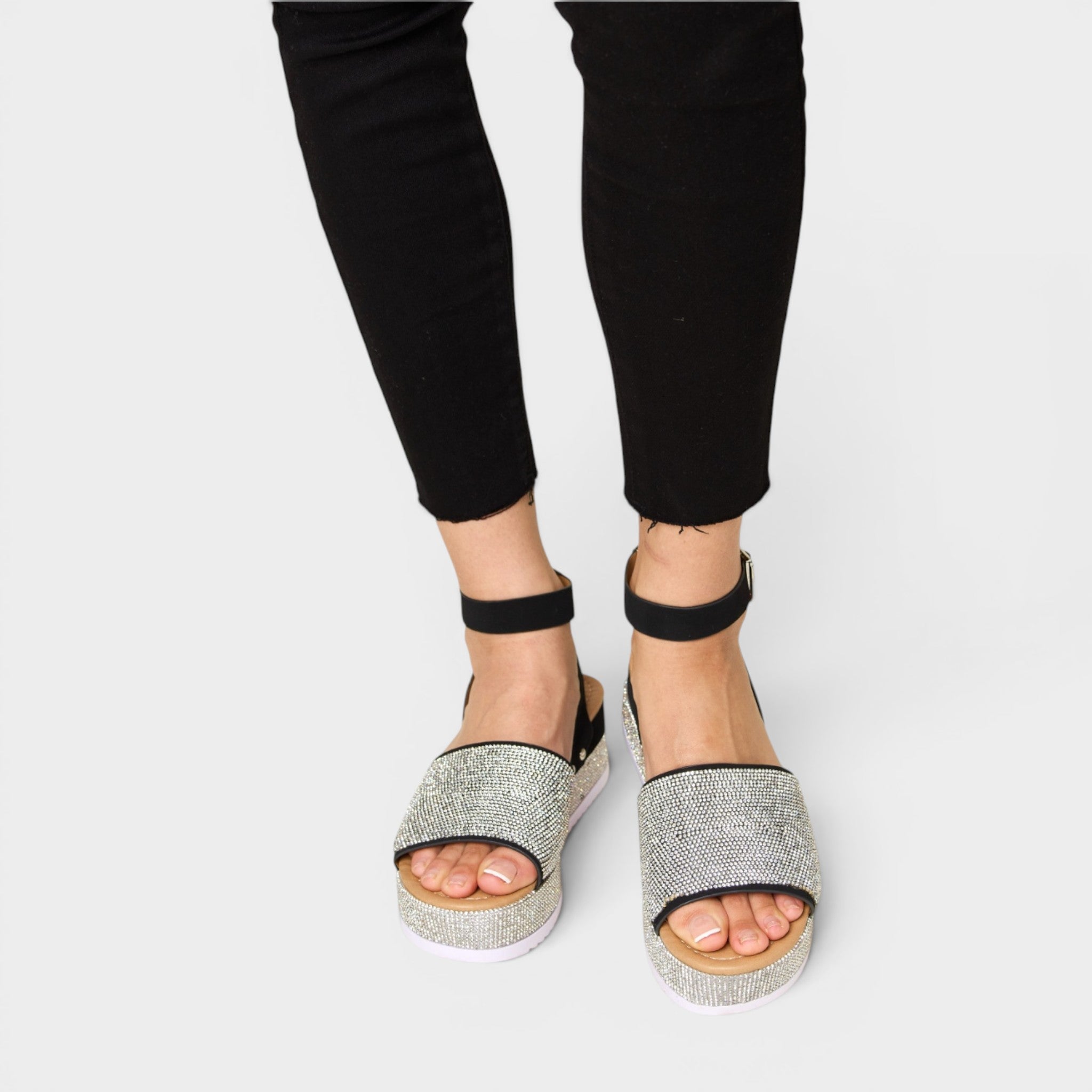 Black sandals with glittery sole worn by a person on a white background