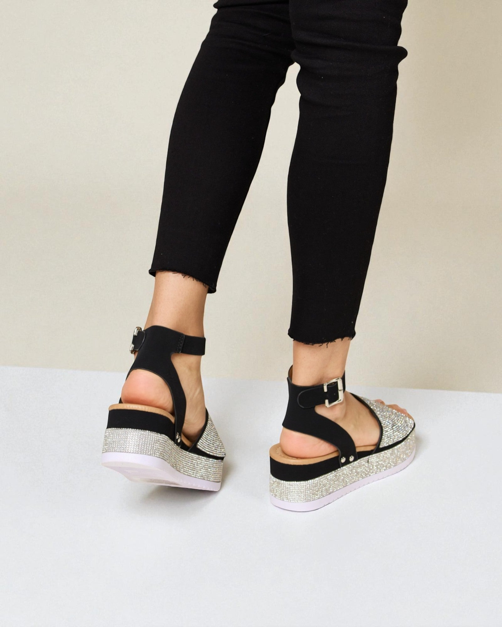 Black sandals with glitter sole worn with black pants on a white background