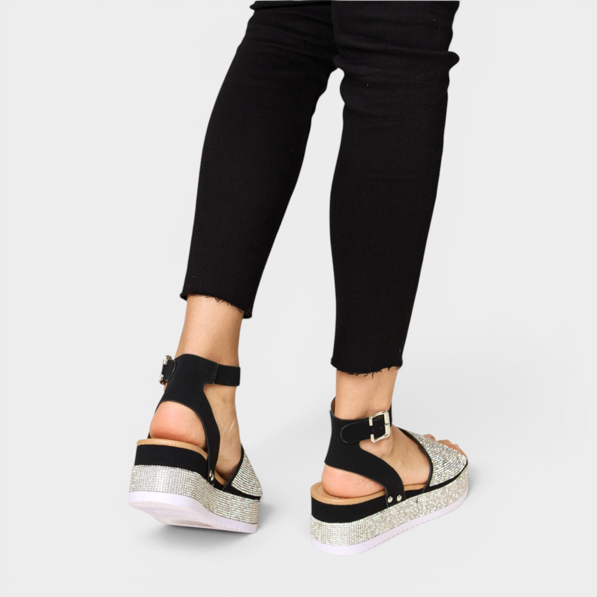Black sandals with glittery sole worn with black pants on a light gray background