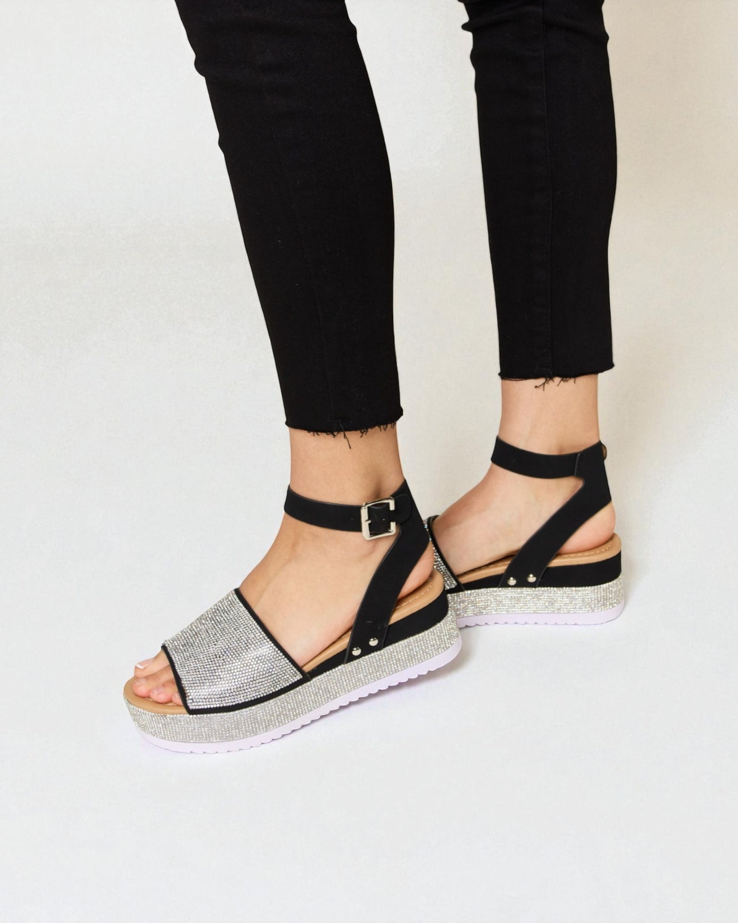 Black sandals with silver glittery straps worn with black pants on a white background