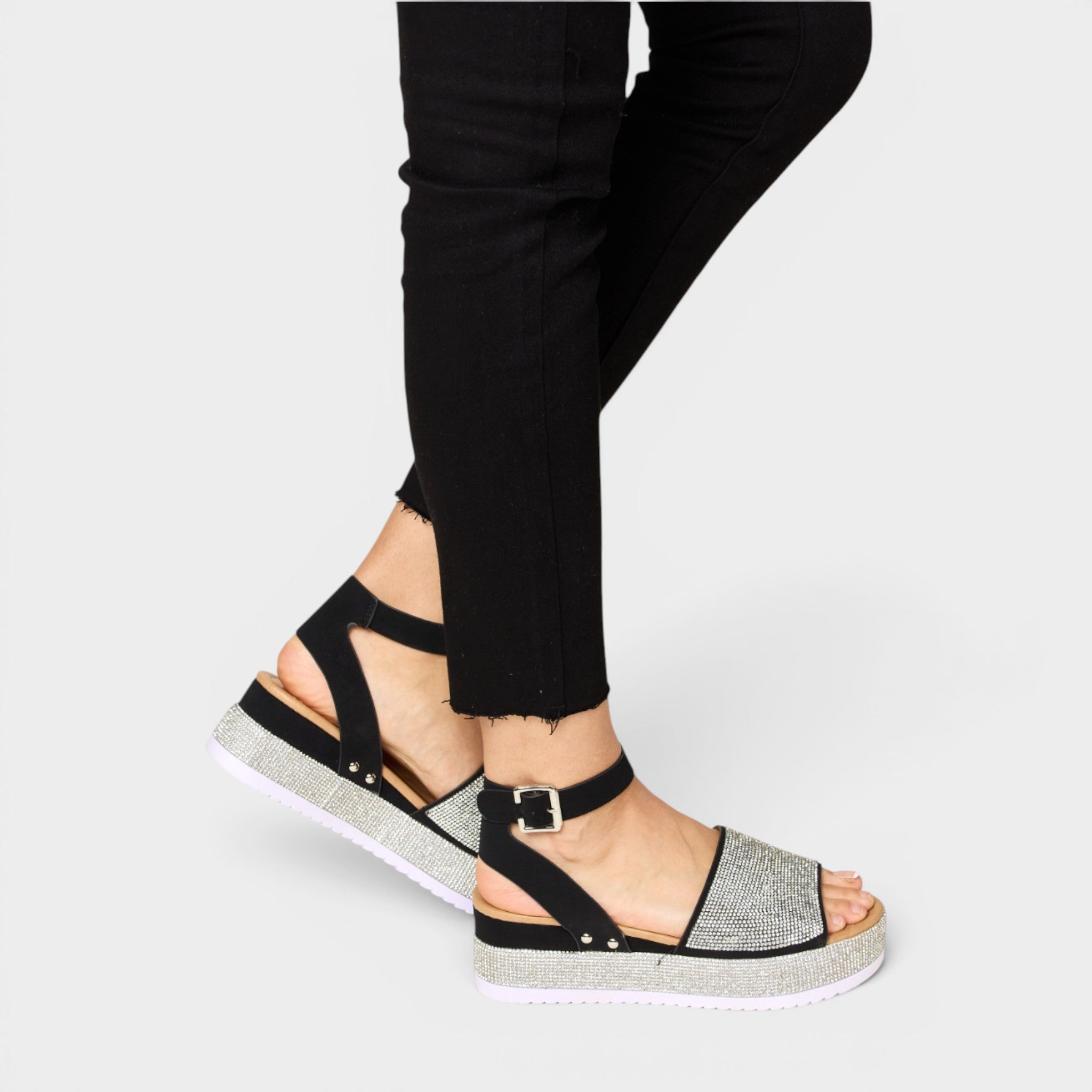Black strappy sandal with a platform sole worn with black pants on a light gray background