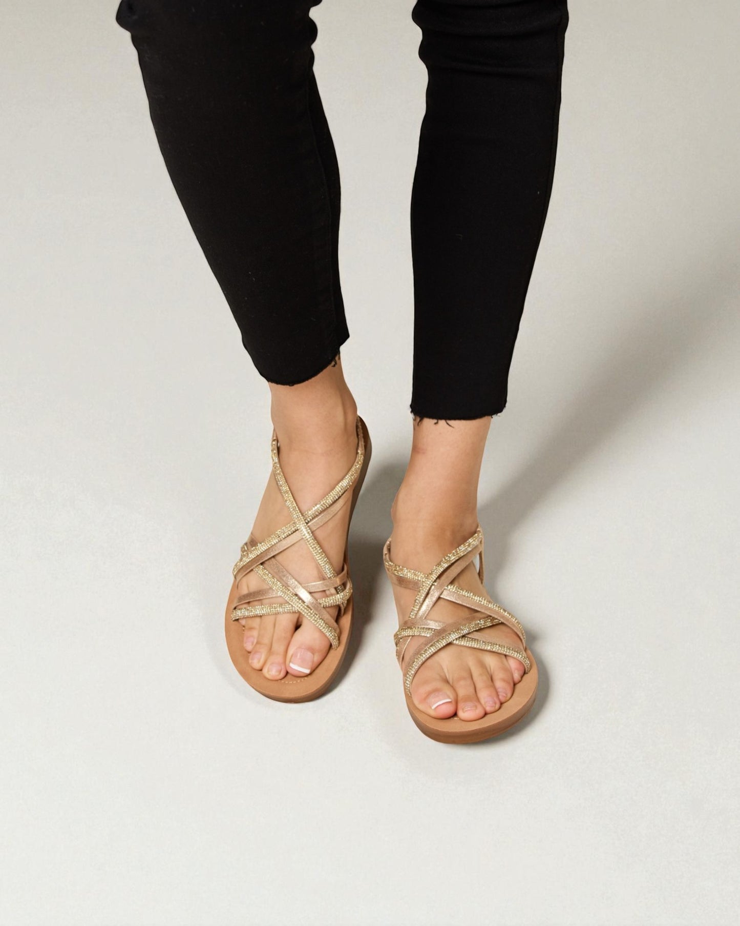 Person wearing gold strappy sandals on a plain background
