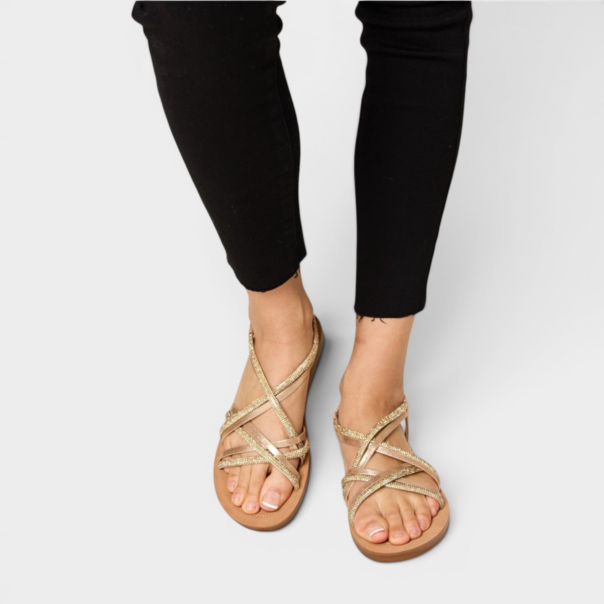 Gold strappy sandals worn with black pants on a white background