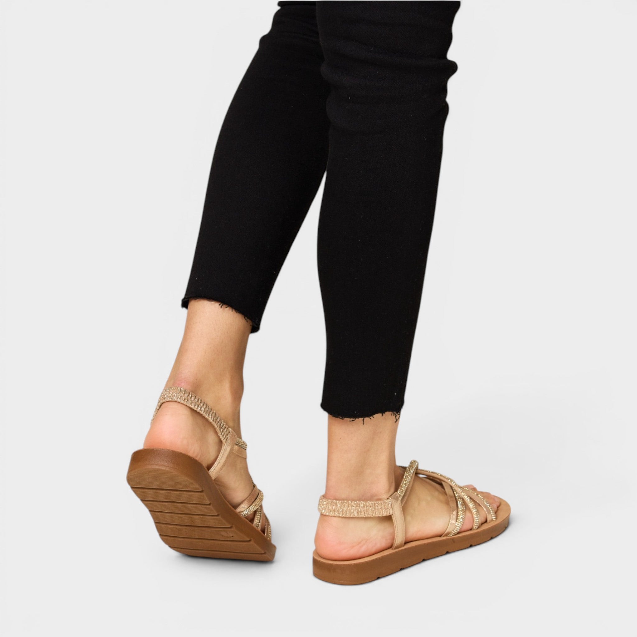 Beige sandals worn with black pants on a light gray background