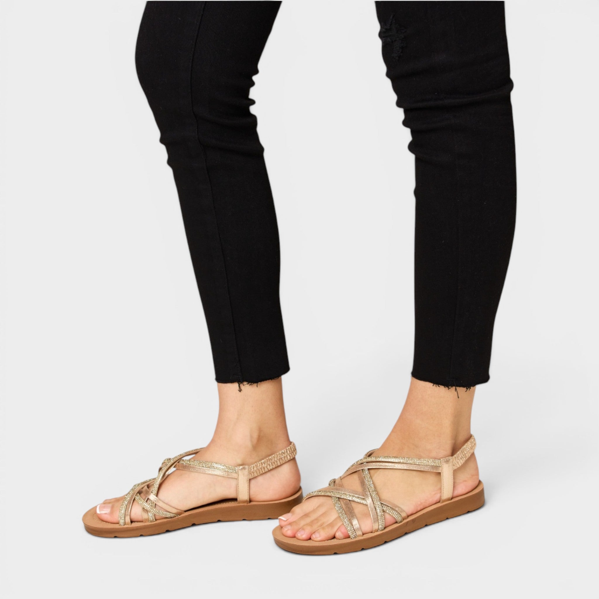 Gold strappy sandals worn with black pants on a white background