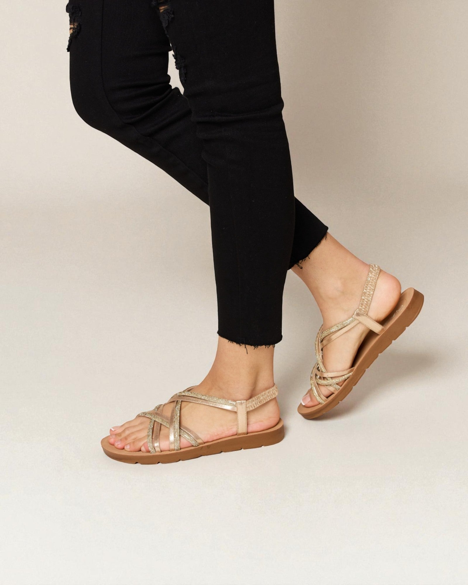 Person wearing gold sandals on a plain background