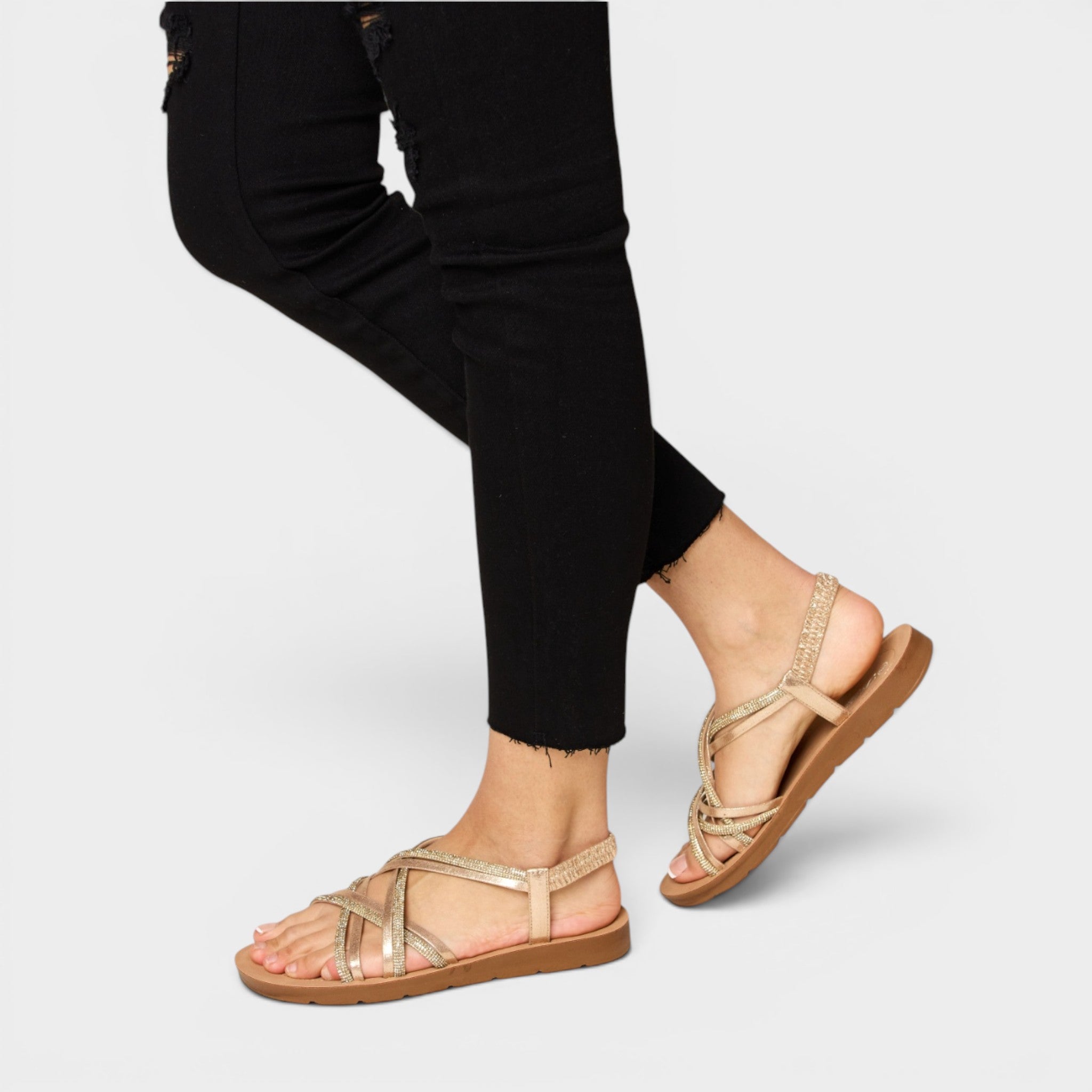Person wearing gold sandals on a plain background