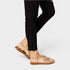 Person wearing gold sandals and black pants on a white background