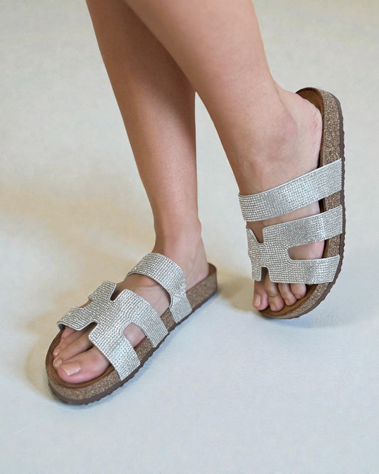 Silver sandals with cork sole worn by a person on a light background