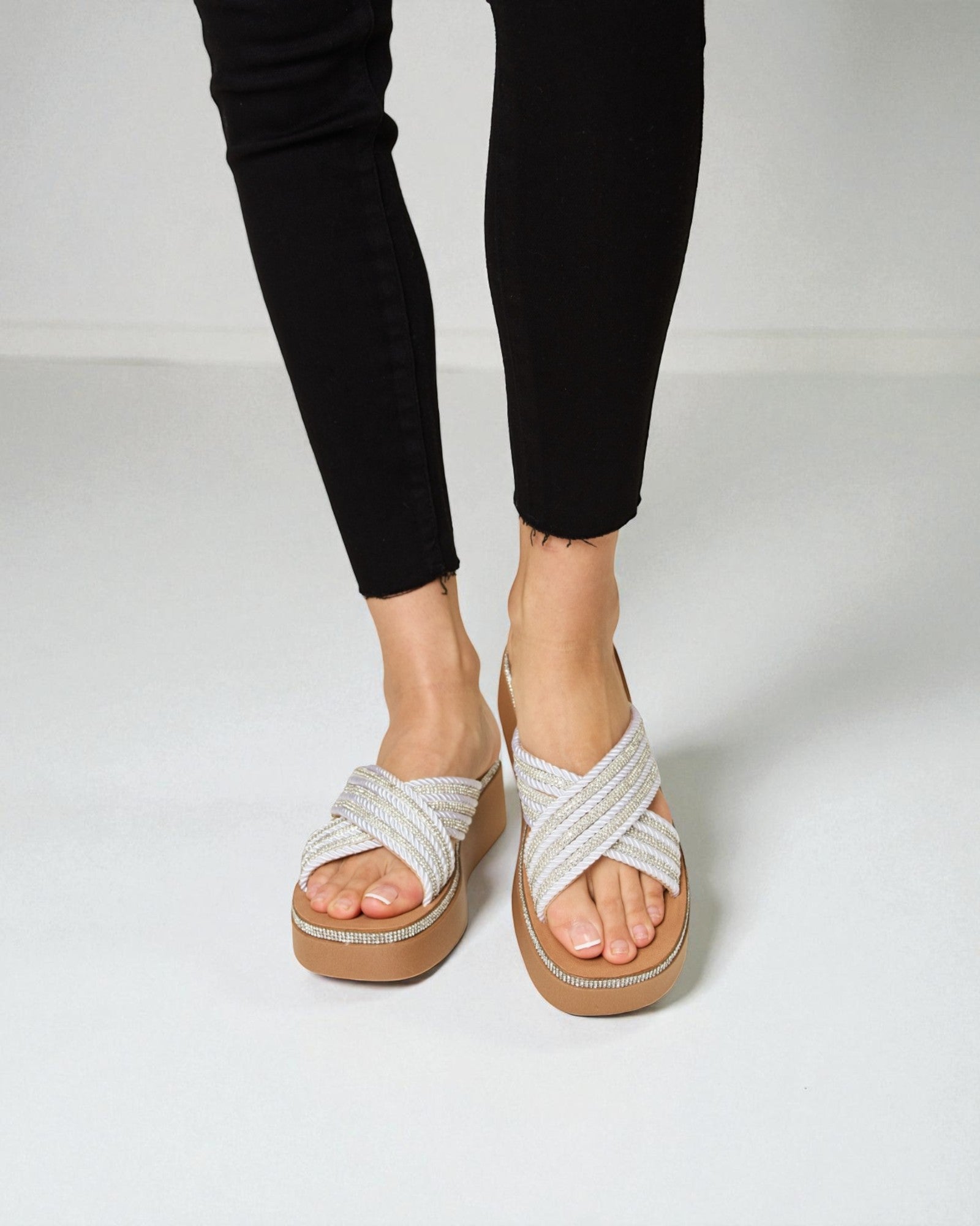 White sandals with criss-cross straps worn with black pants on a white background