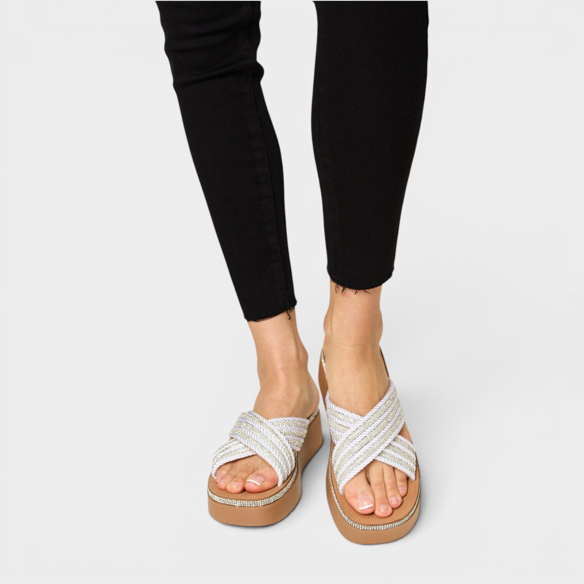 White sandals with brown soles worn with black pants on a light gray background
