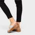 Brown sandal with criss-cross straps worn by a person in black pants on a light gray background