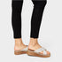 White sandals with brown soles worn with black pants on a light gray background