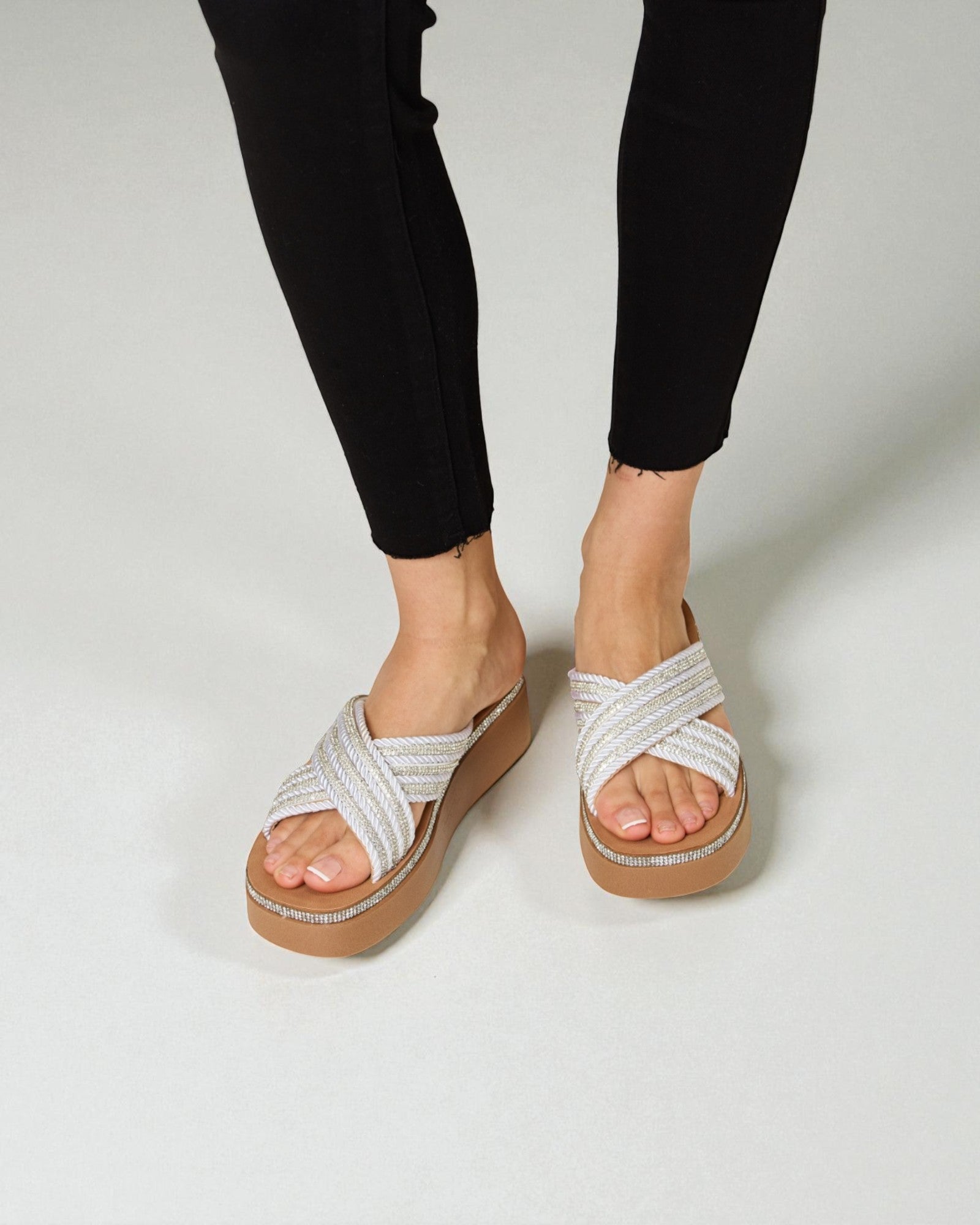 White sandals with brown soles worn by a person in black leggings on a light gray background