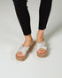 White sandals with brown soles worn by a person in black leggings on a light gray background