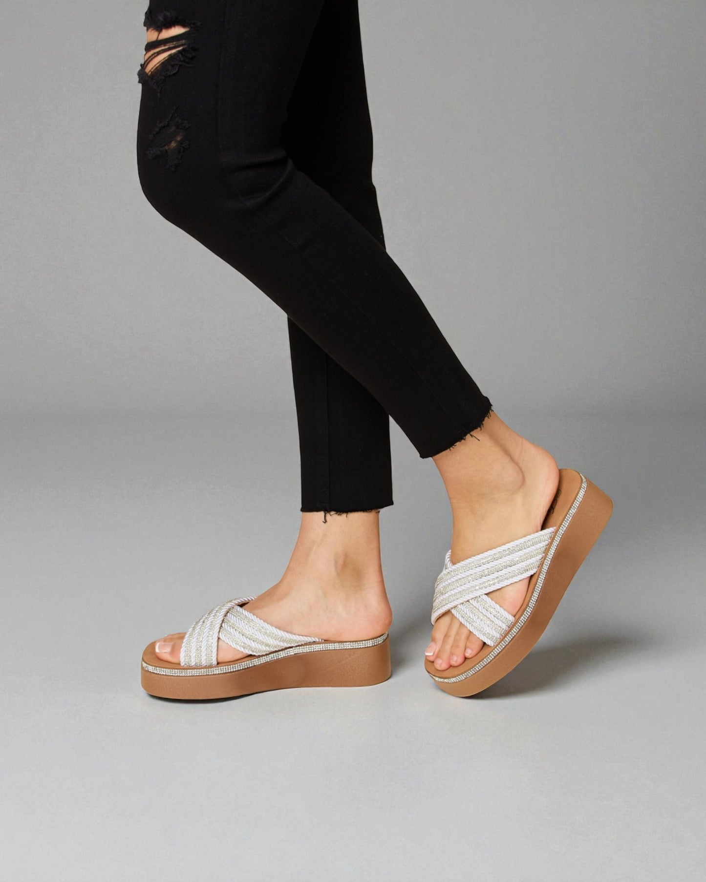 White sandals worn with black pants on a gray background