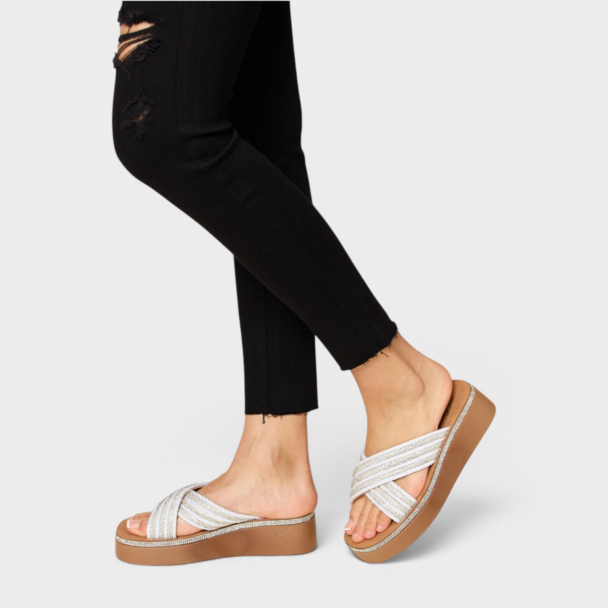 White sandals with brown soles worn by a person on a light gray background