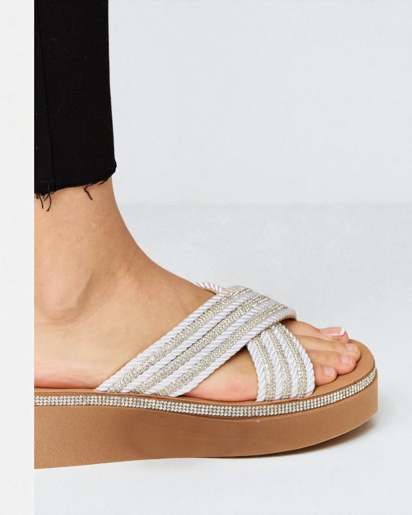 White sandal with brown sole worn by a person on a white background