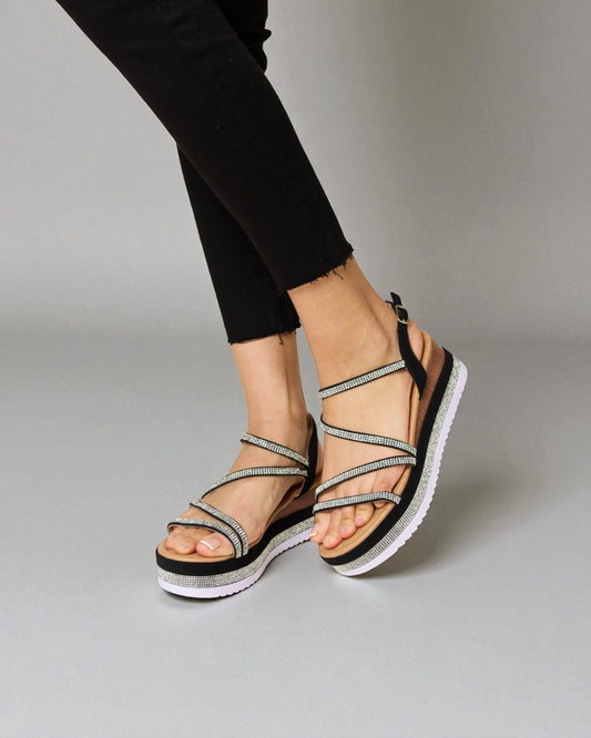 Black sandals with multiple straps worn by a person on a gray background