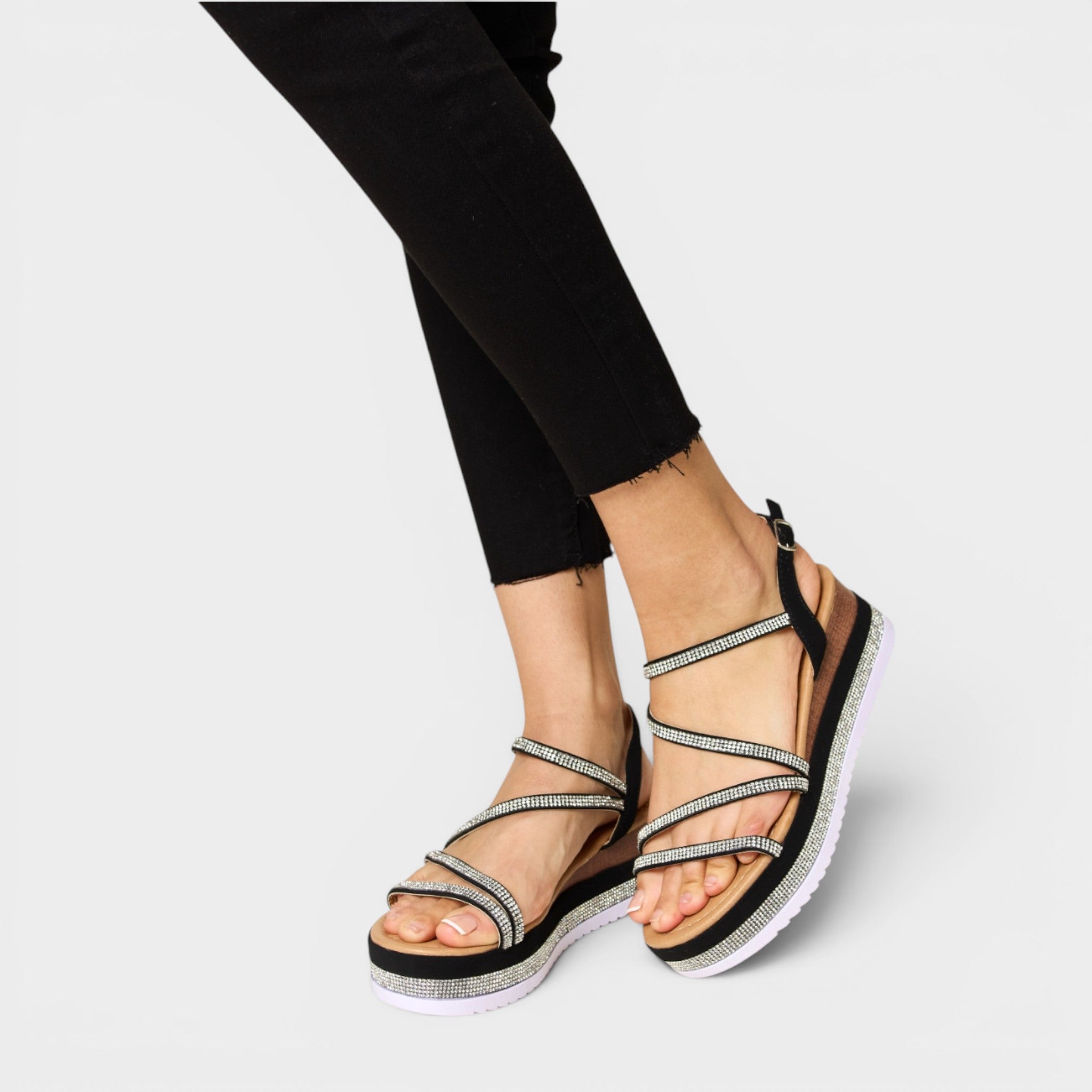 Black and silver strappy sandals worn with black pants on a light gray background