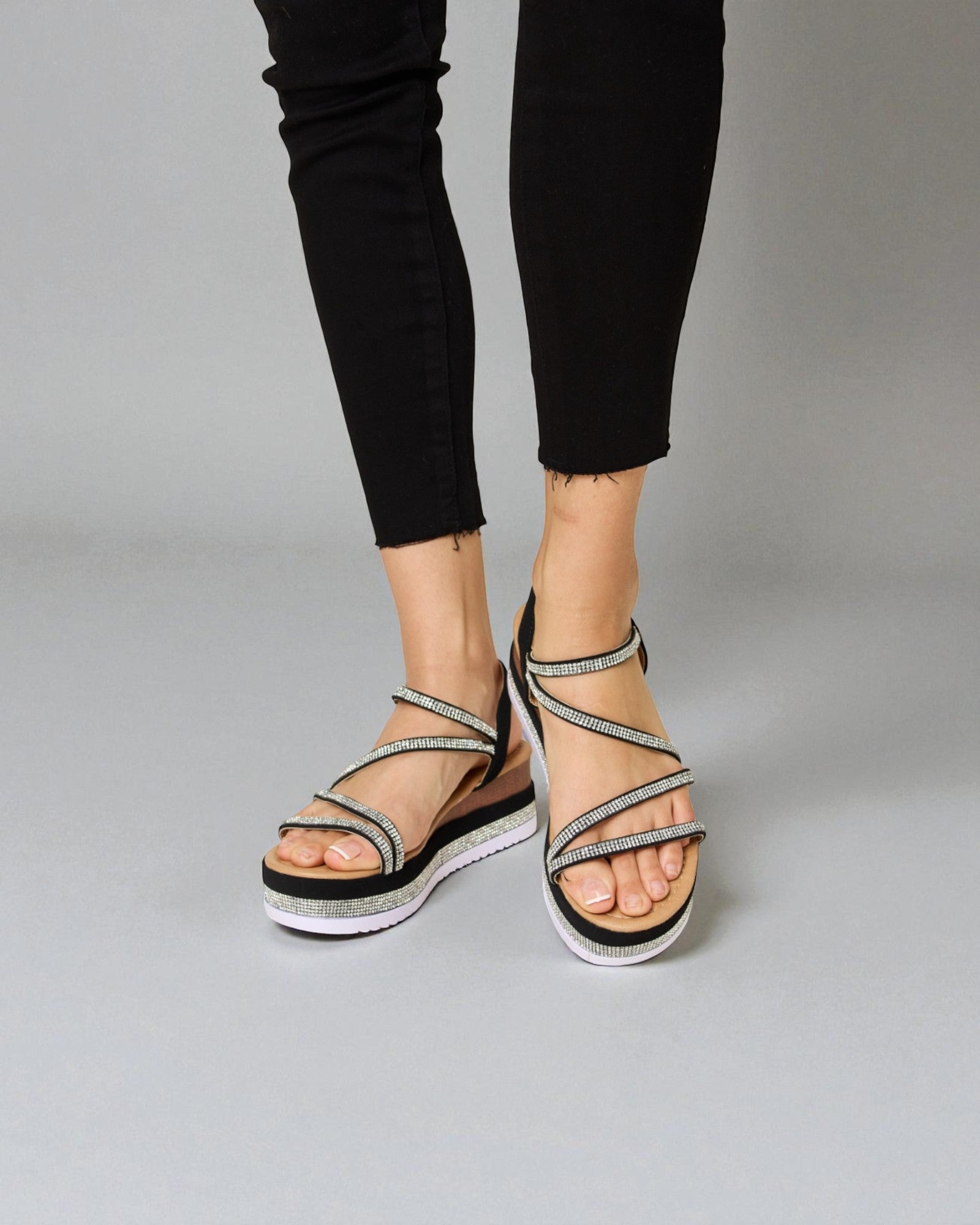 Black sandals with thin straps worn by a person on a gray background