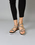 Black sandals with thin straps worn by a person on a gray background