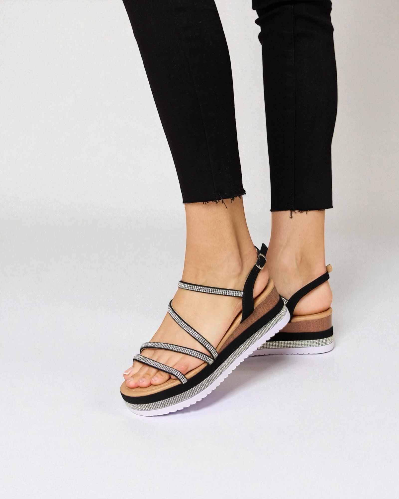 Black sandals with metallic straps worn by a person on a light gray background