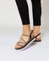 Black sandals with metallic straps worn by a person on a light gray background