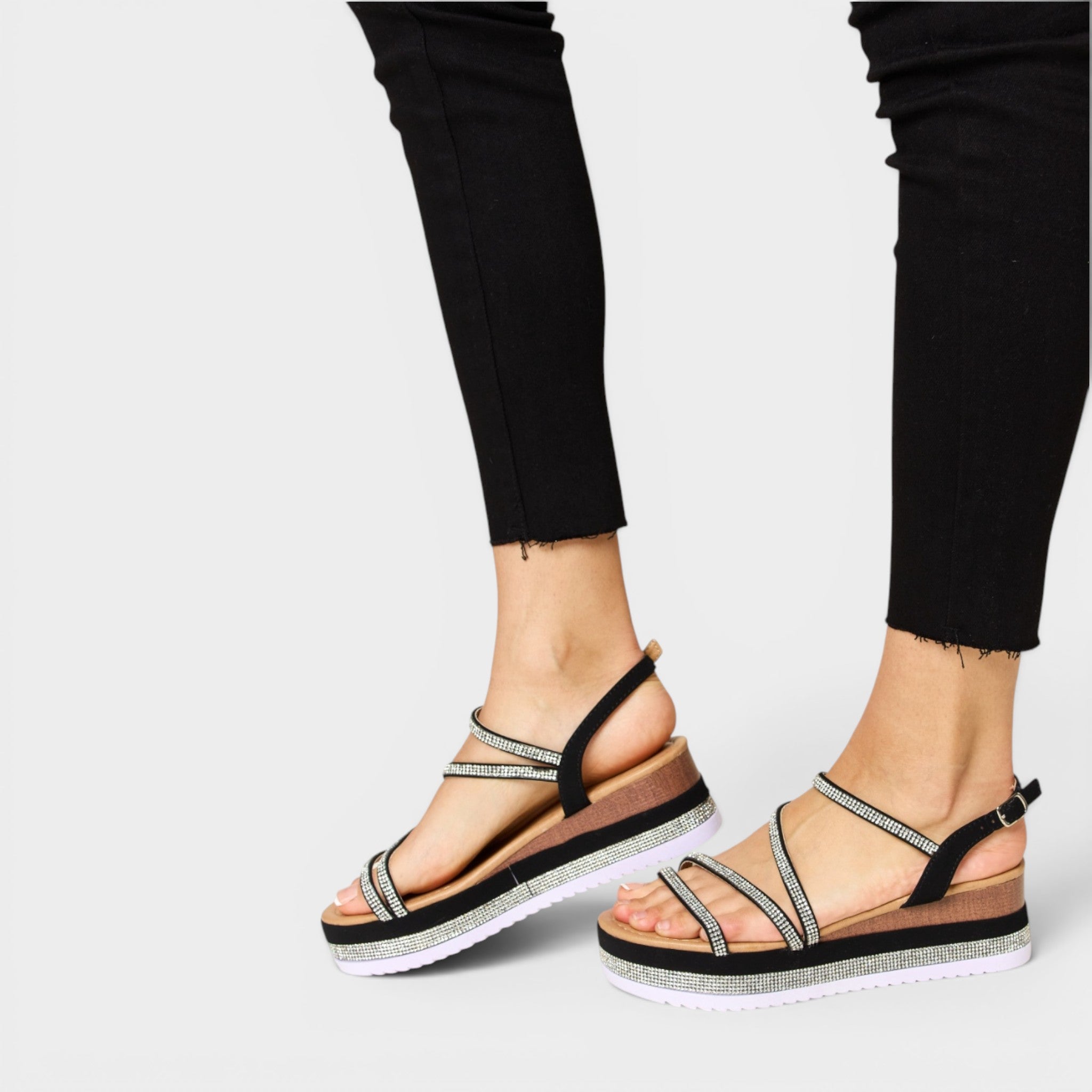 Black sandals with thin straps worn by a person on a light gray background
