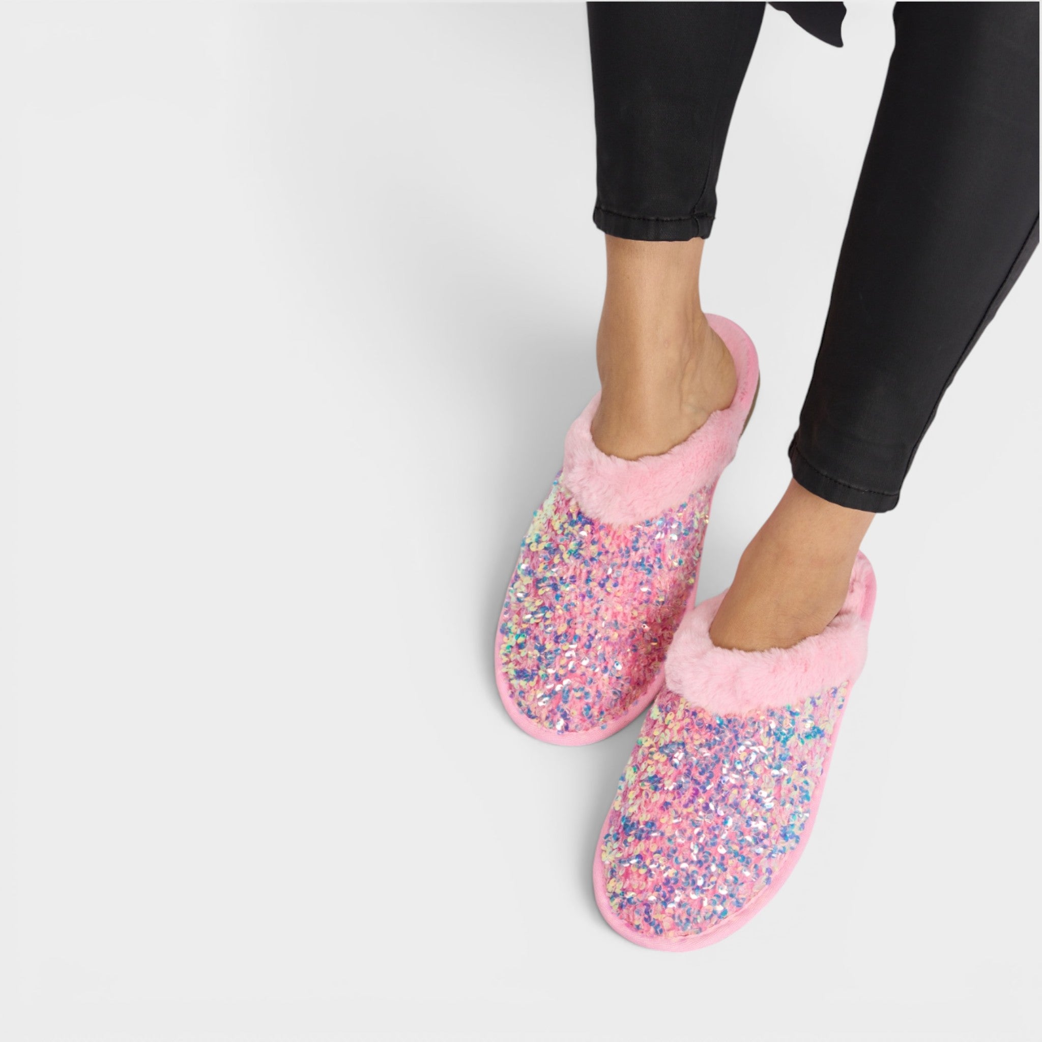 Pink slippers with glitter sole worn by a person on a light gray background