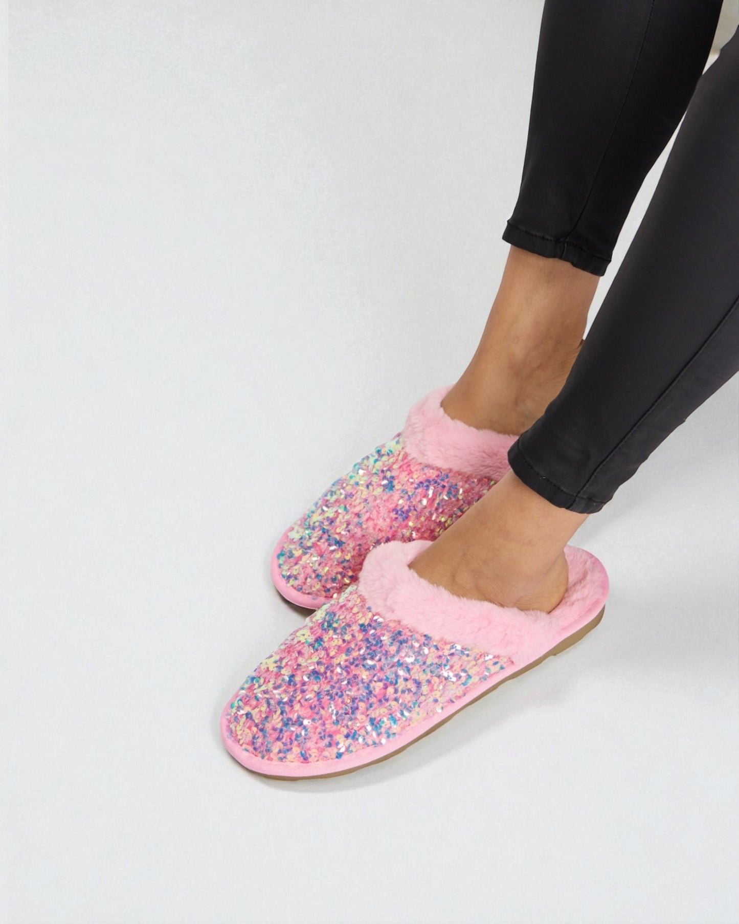 Pink slippers with multicolored sequins worn by a person on a white background