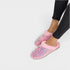 Pink slippers with colorful sequins worn by a person on a white background
