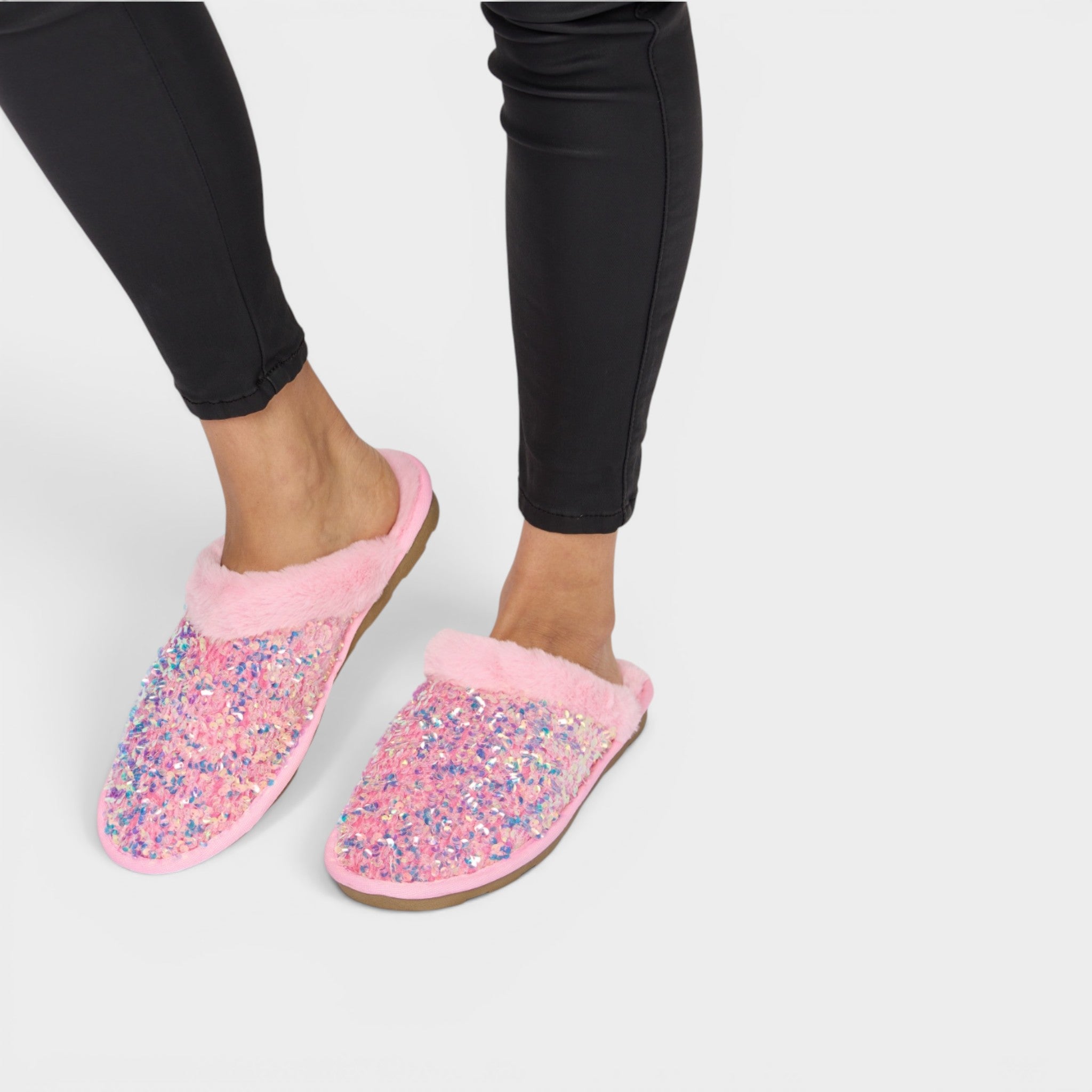 Pink slippers with glitter sole worn by a person on a light gray background