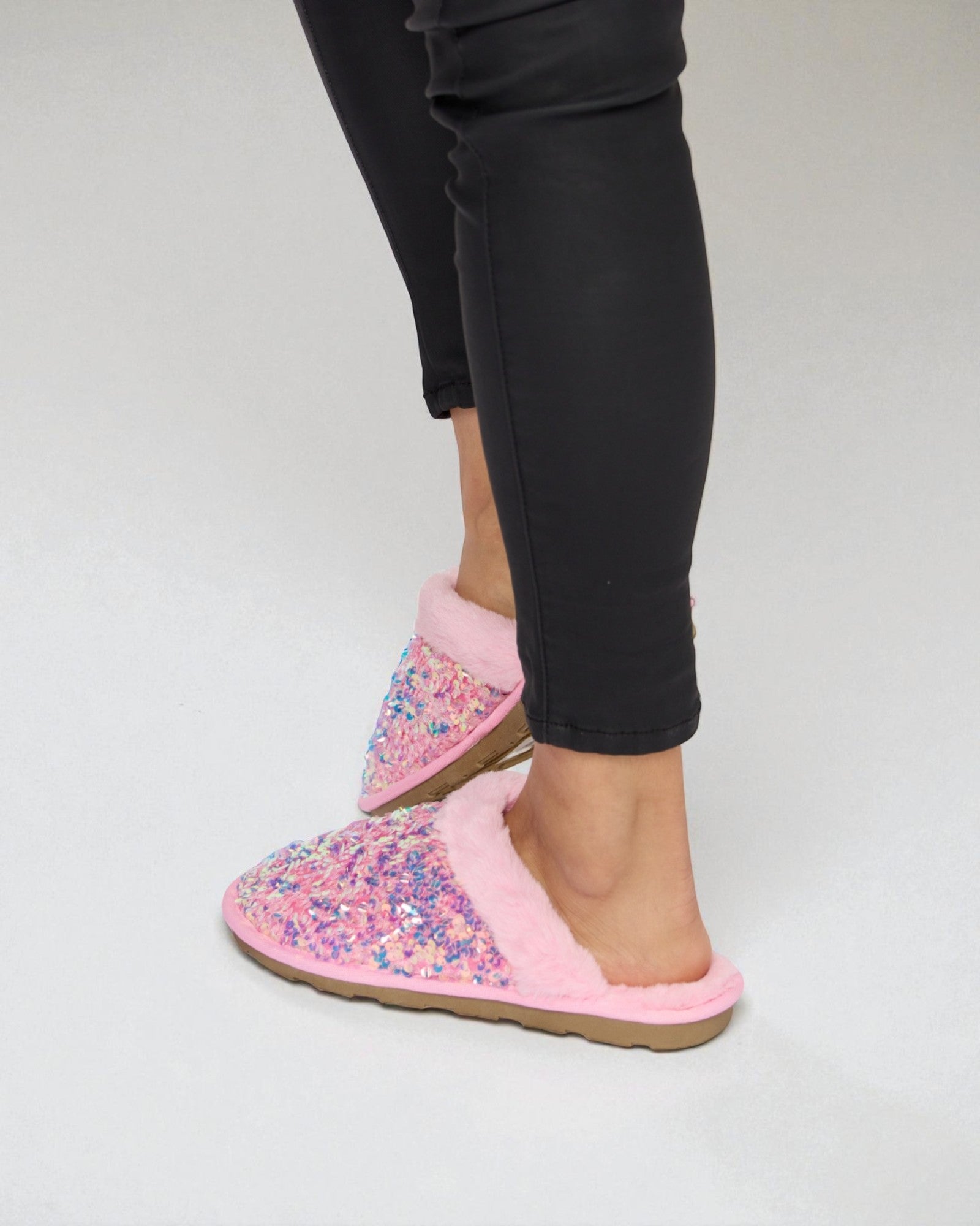 Pink floral slippers worn with black pants on a white background