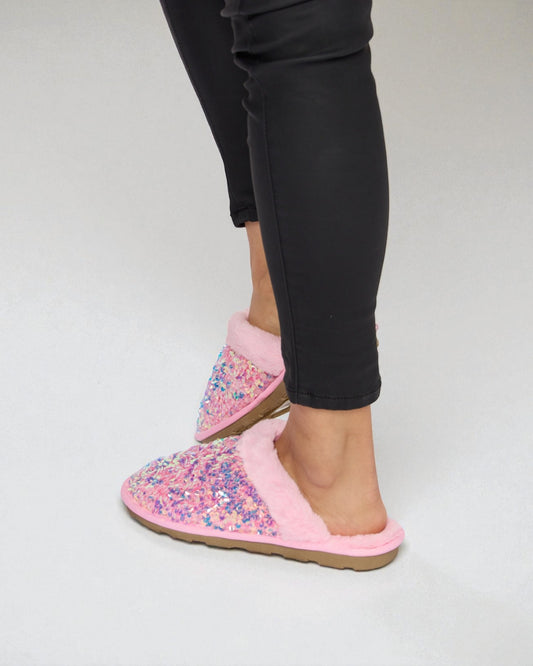Pink floral slippers worn with black pants on a white background