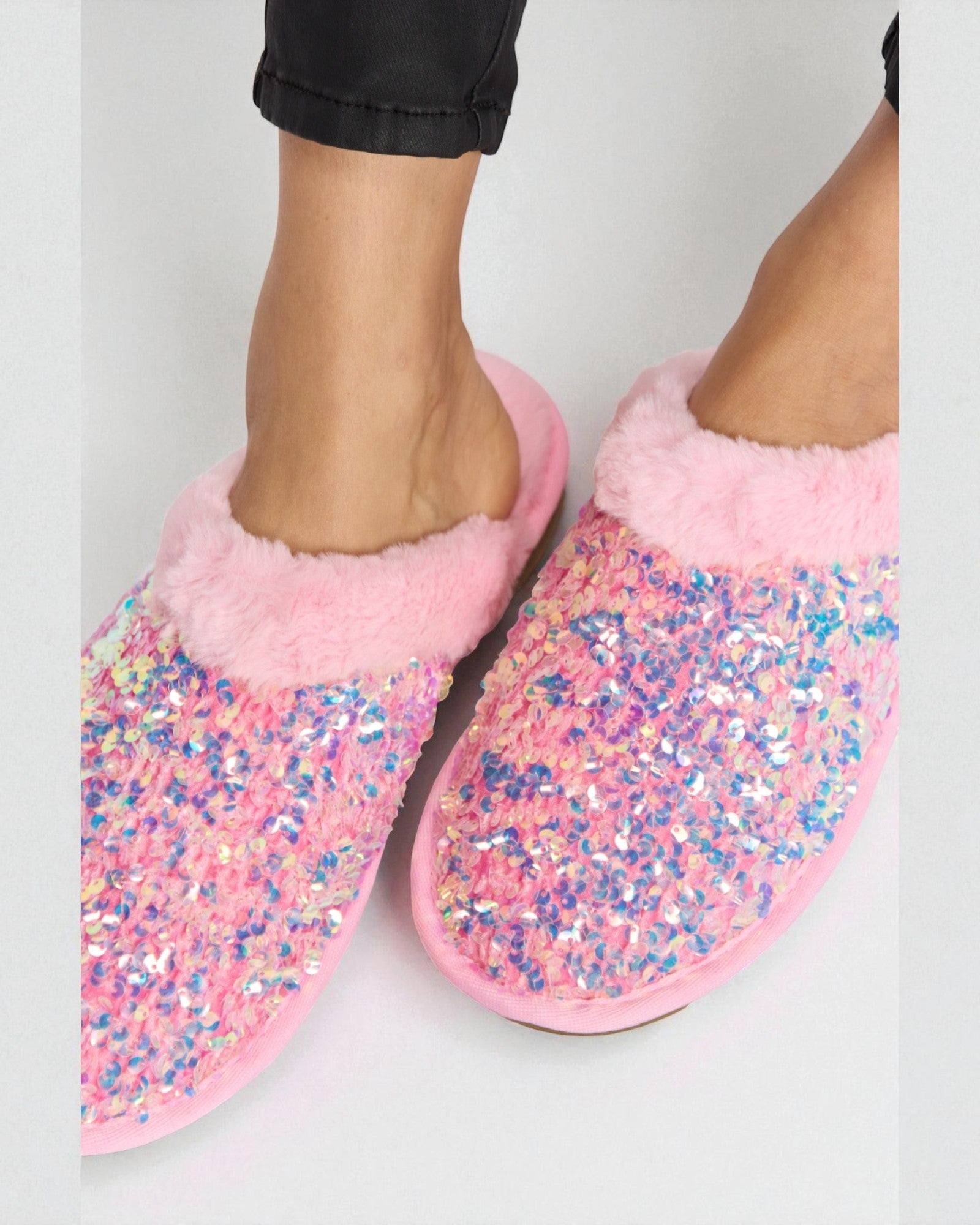 Pink slippers with glitter sole worn by a person on a light gray background