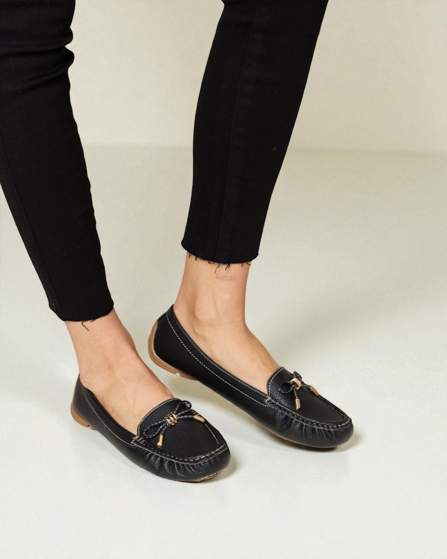 Black loafers worn with black pants on a light background