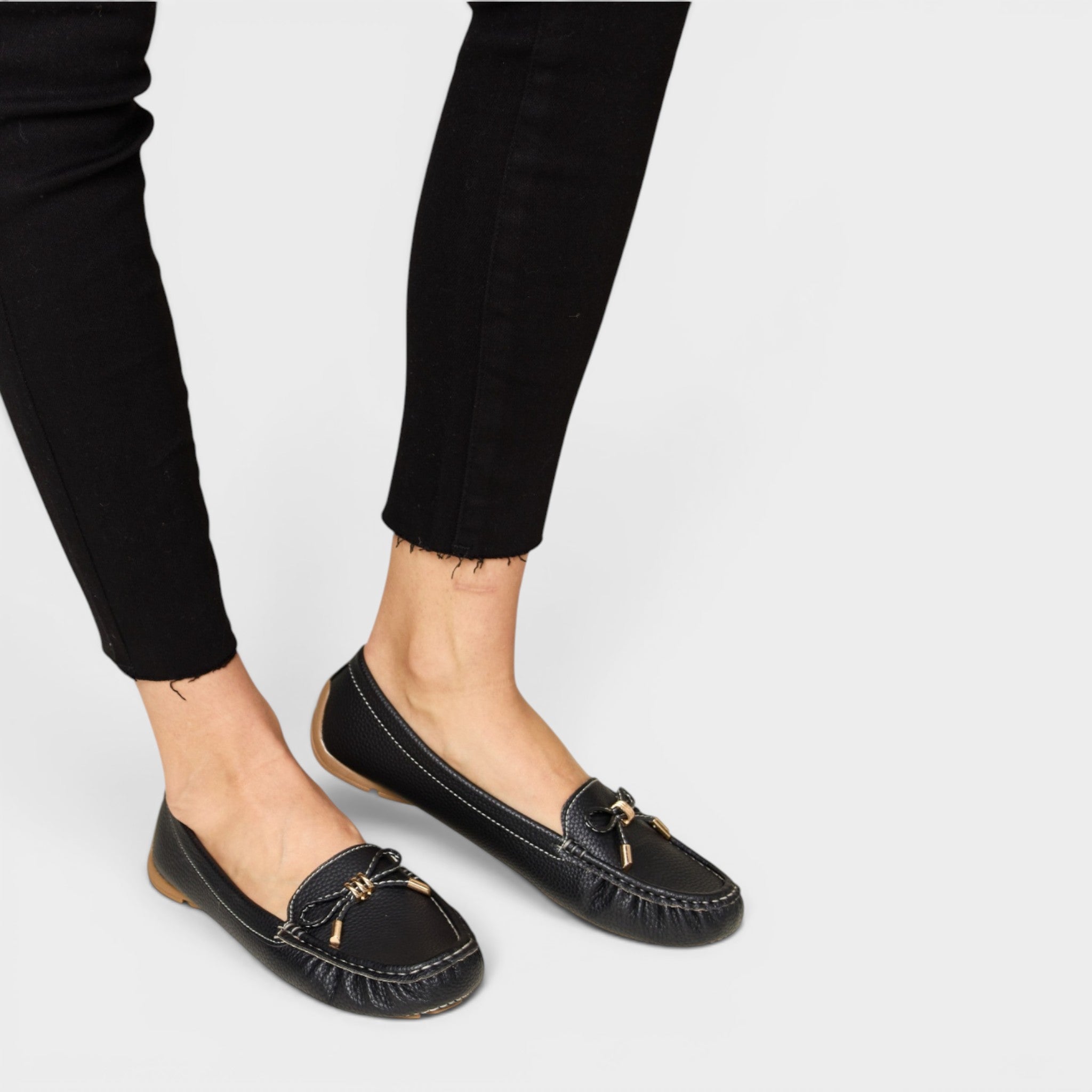 Black loafers worn with black pants on a light gray background