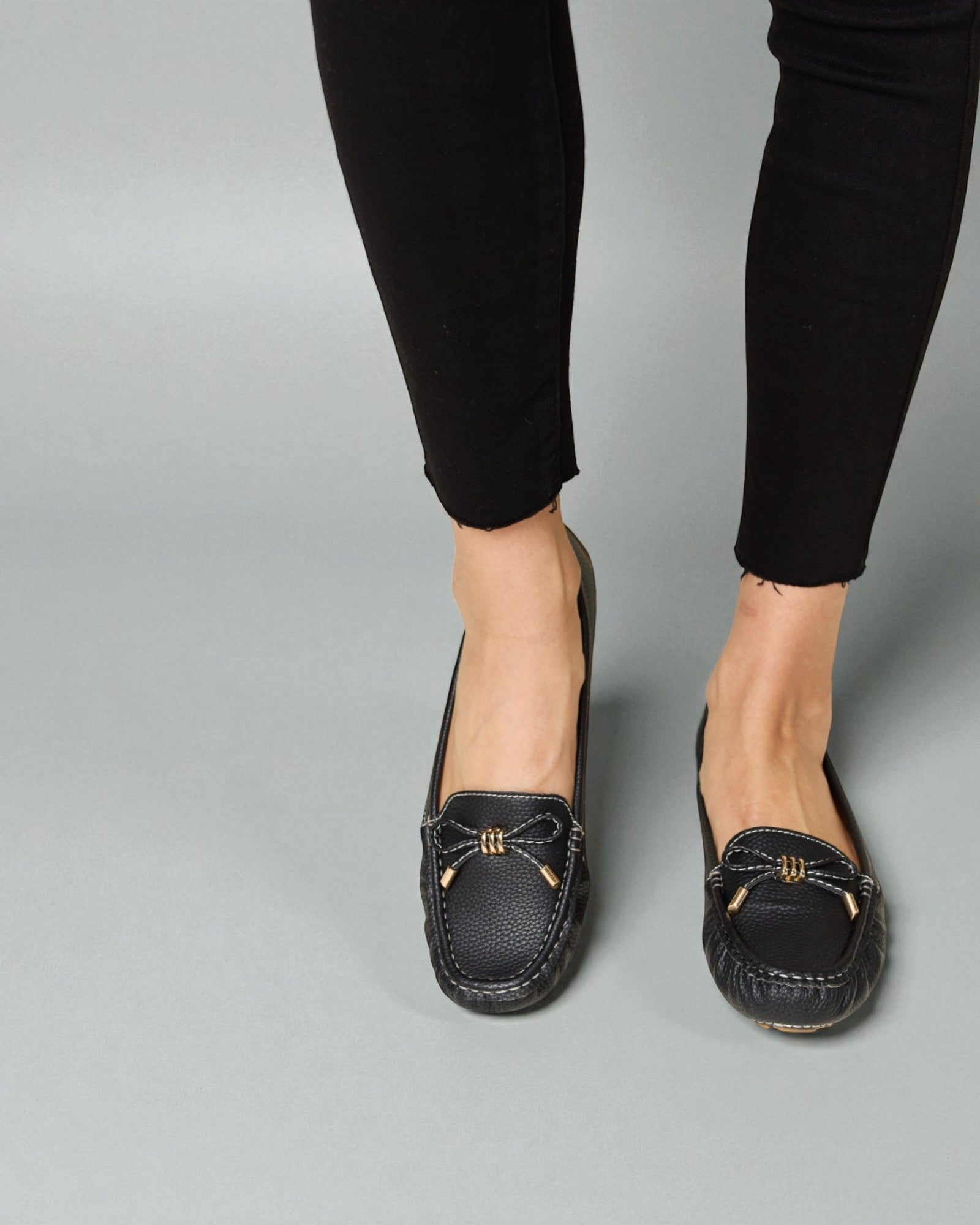 Black loafers worn with black pants on a gray background