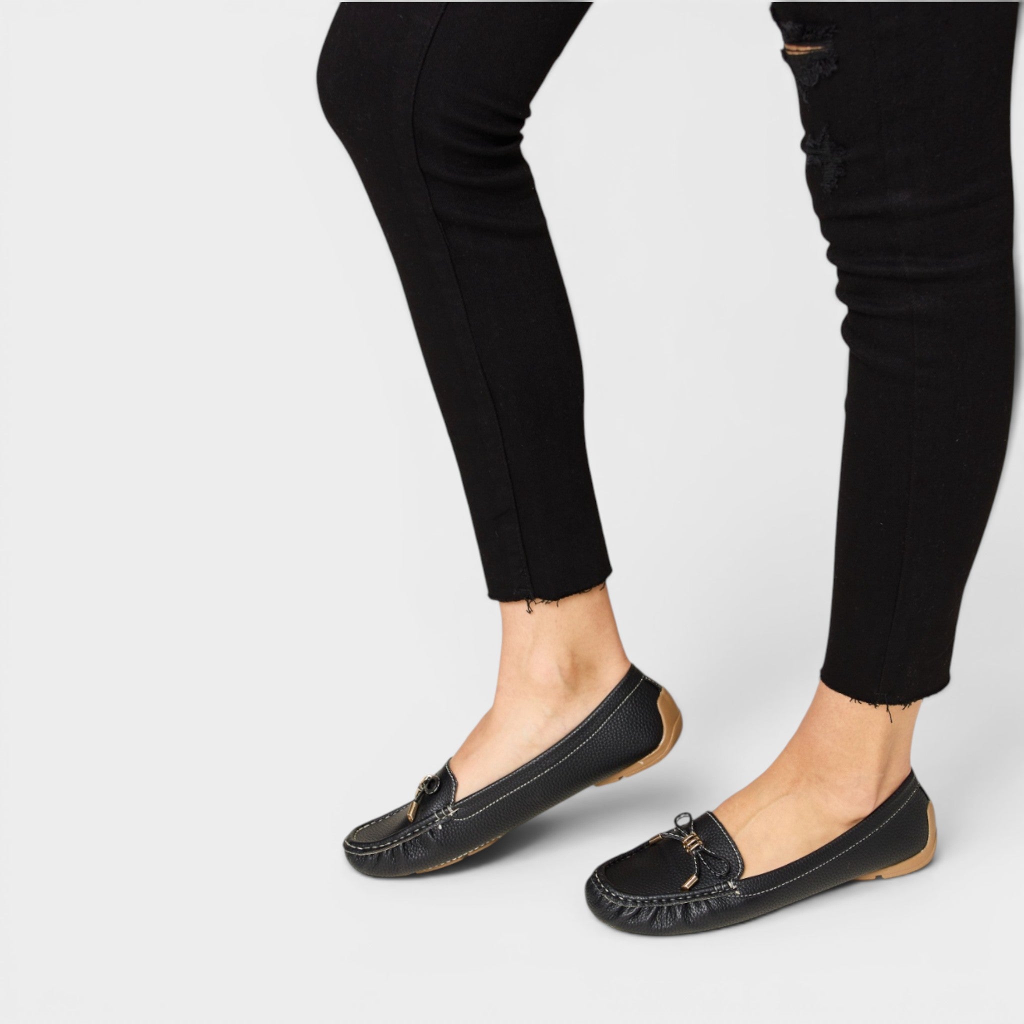 Black loafers worn with black pants on a light gray background