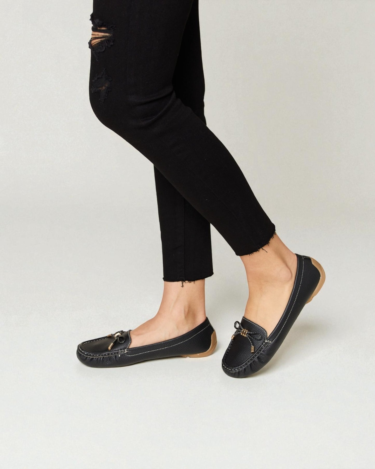 Person wearing black loafers and black pants on a light gray background