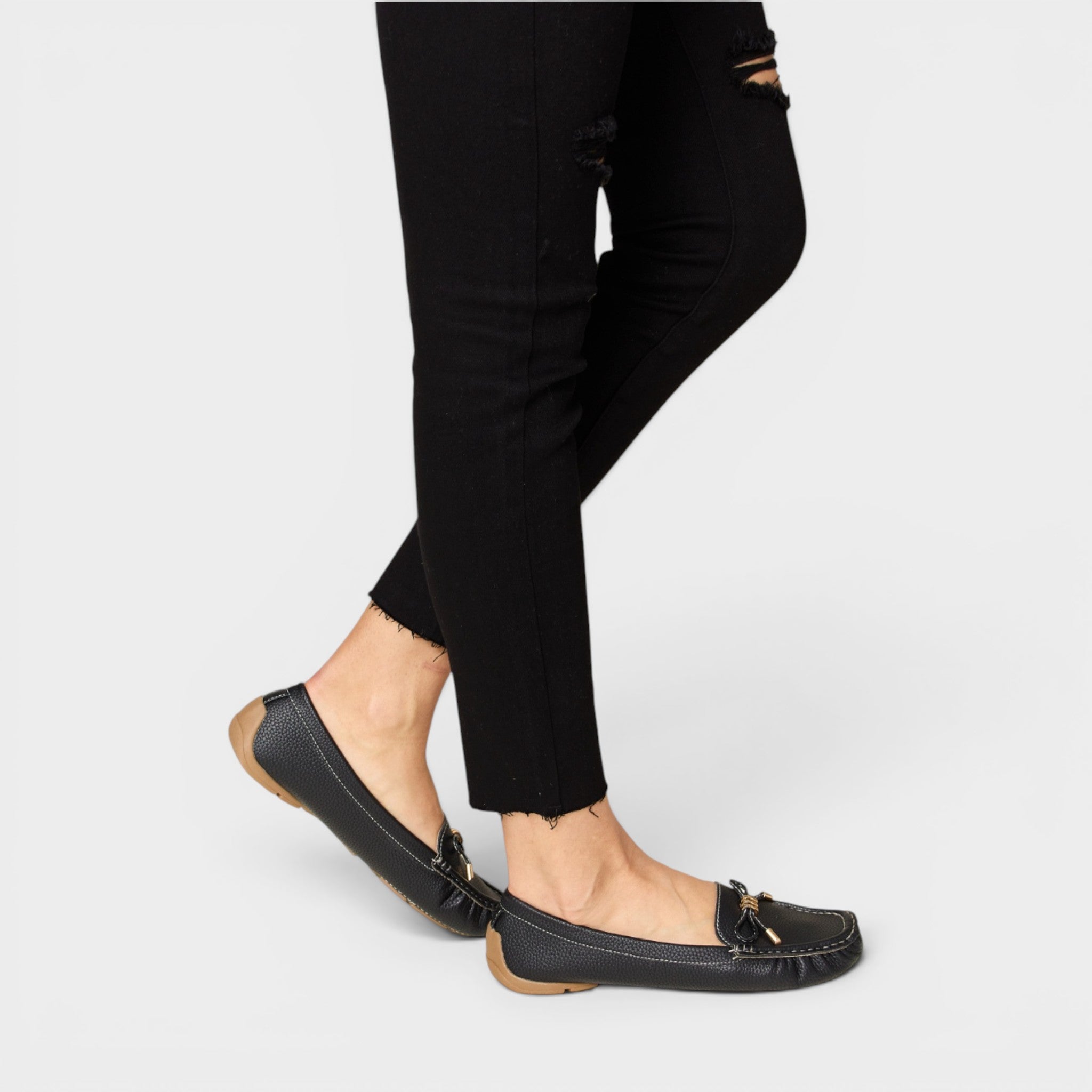 Black flat shoes worn with black pants on a white background