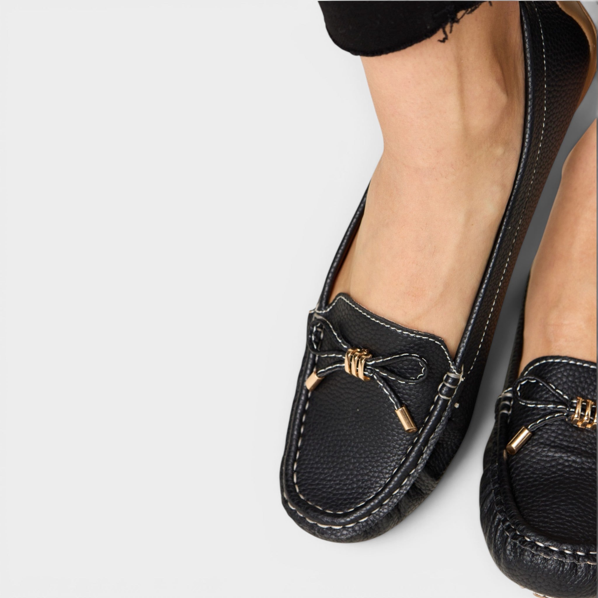 Black loafers with gold accents worn by a person on a light gray background