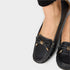 Black loafers with gold accents worn by a person on a light gray background
