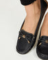 Black loafers with gold accents worn by a person on a light gray background